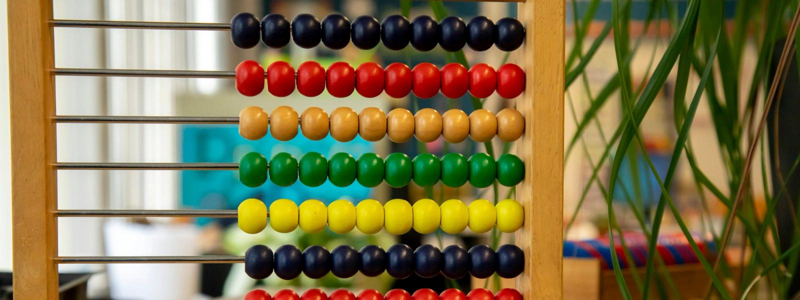 A wooden bead frame with rows of coloured beads on a classroom table