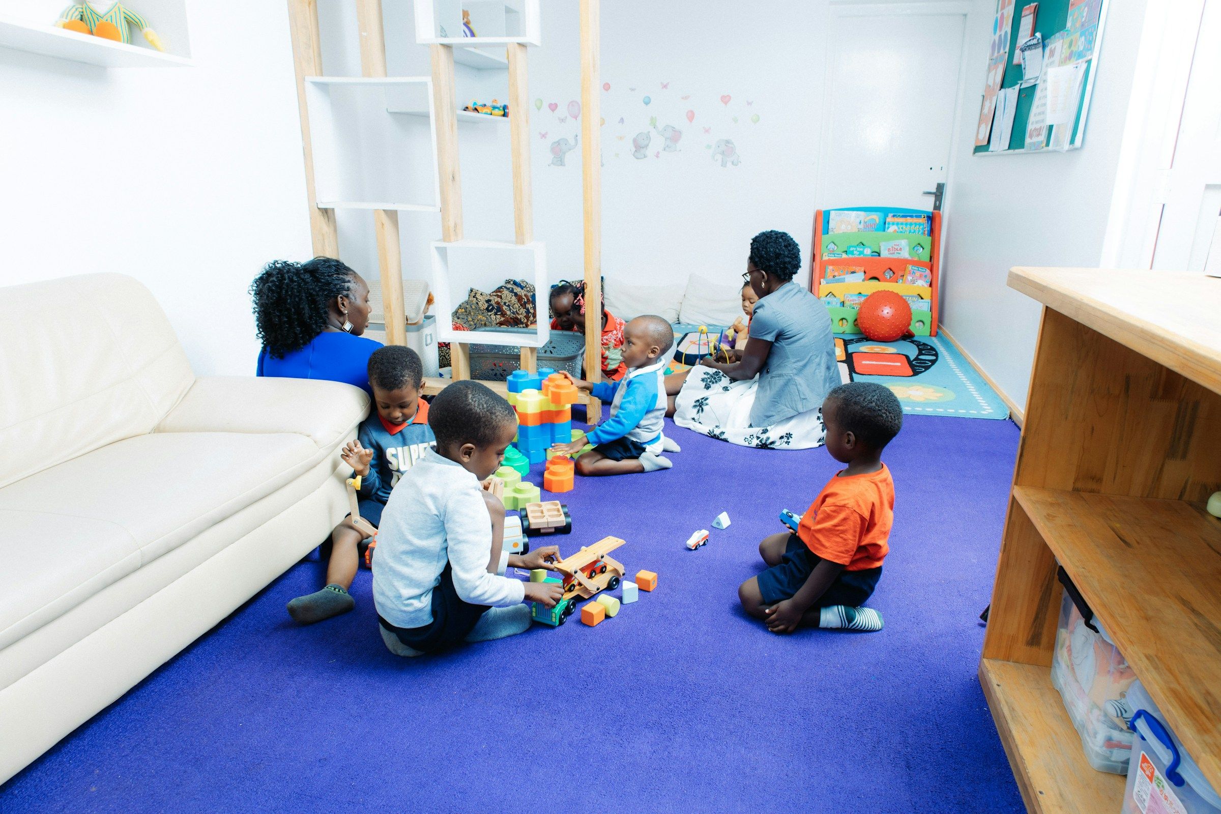 Children at work with wooden blocks and toy vehicles on a classroom rug