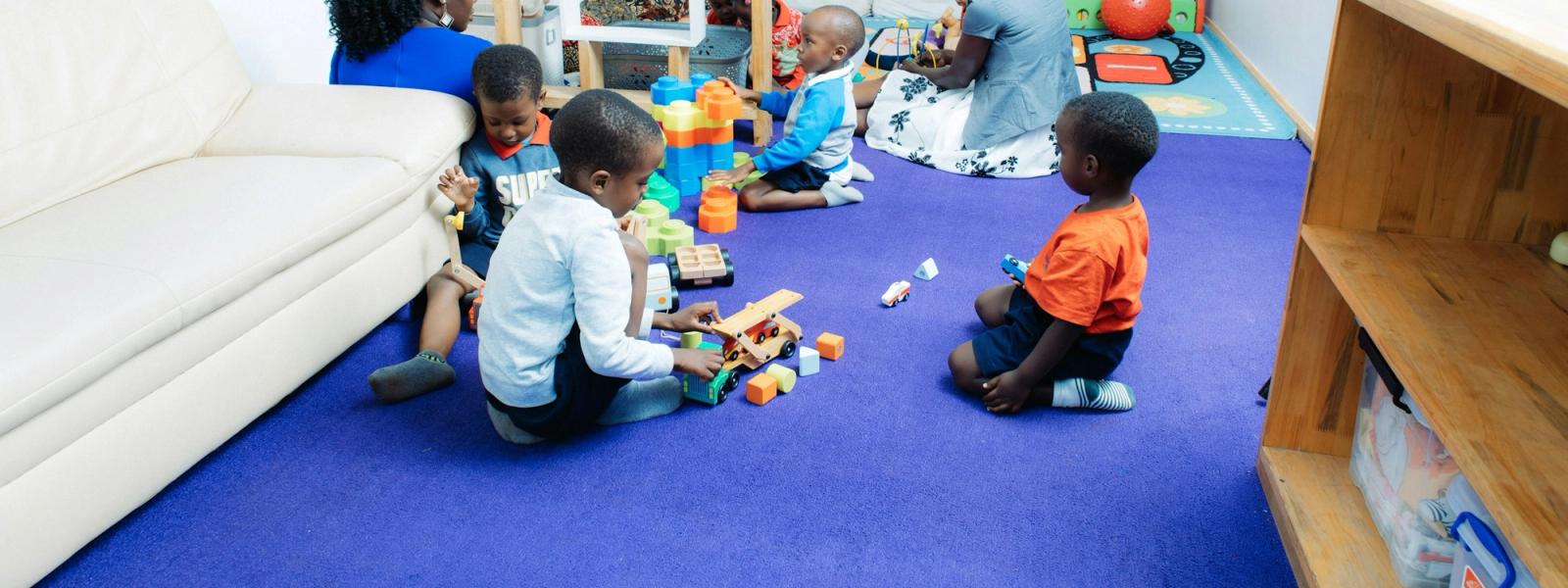 Children at work with wooden blocks and toy vehicles on a classroom rug