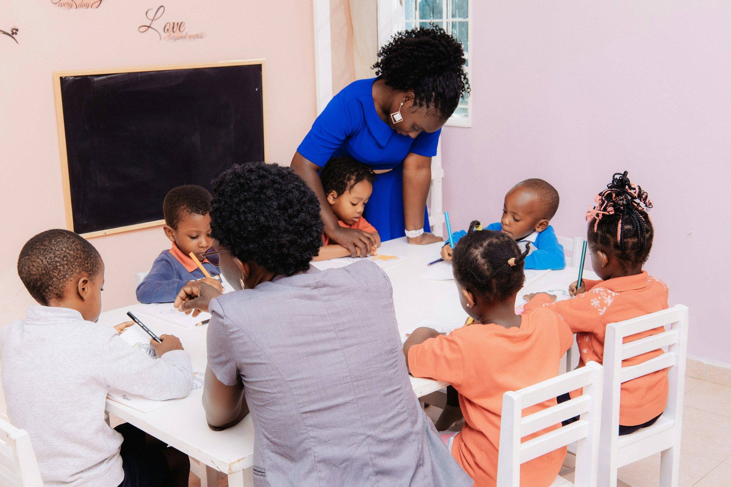 A teacher seated with a group of children drawing at a low table