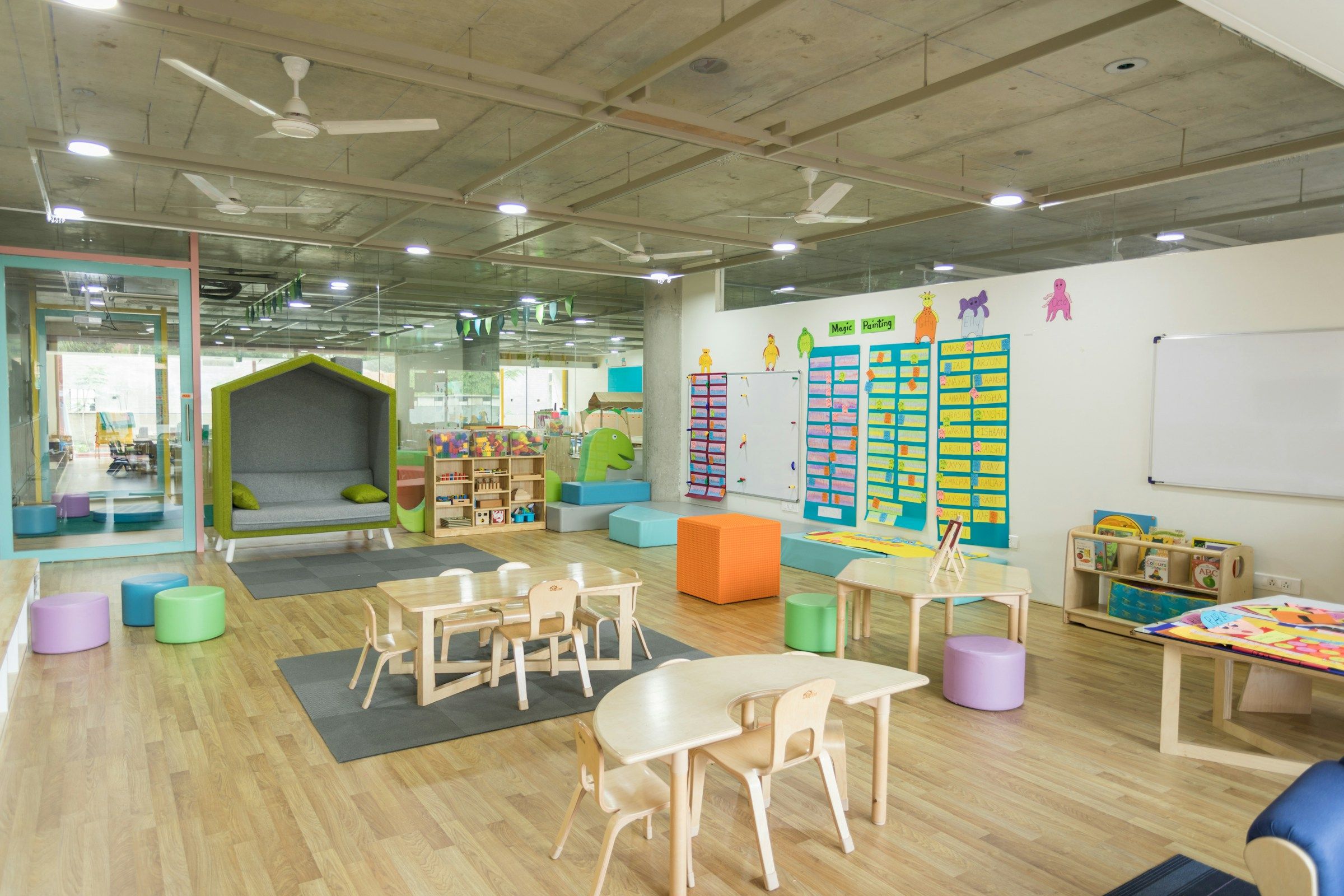 A bright, open classroom with child-height tables, chairs and a reading nook