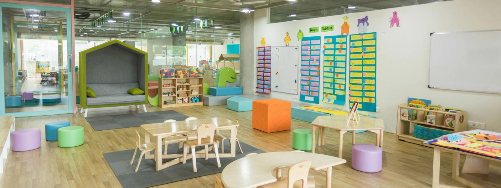 A bright, open classroom with child-height tables, chairs and a reading nook