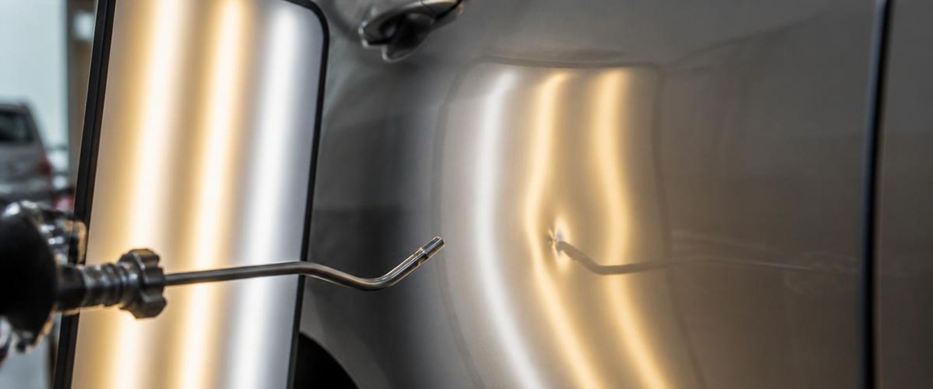 Paintless dent repair rod and reflection board working a shallow dent out of a car door