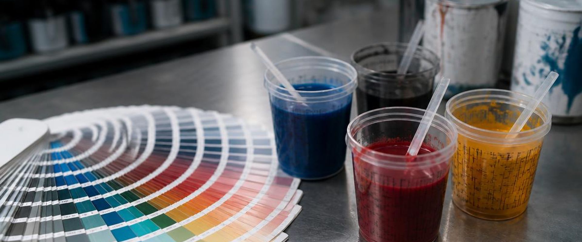 Automotive paint color fan deck beside tinted paint mixing cups on a shop mixing bench
