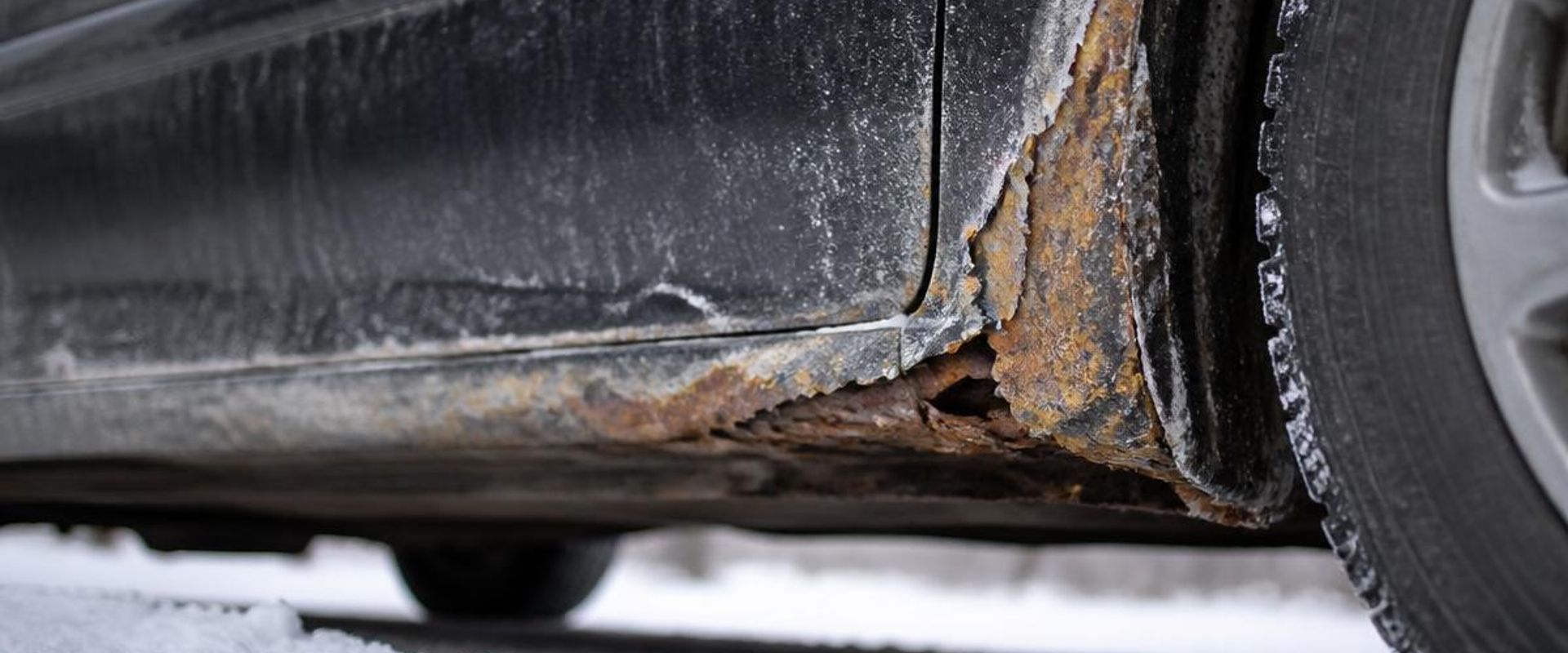 Rust corrosion along a car rocker panel and wheel arch caused by winter road salt