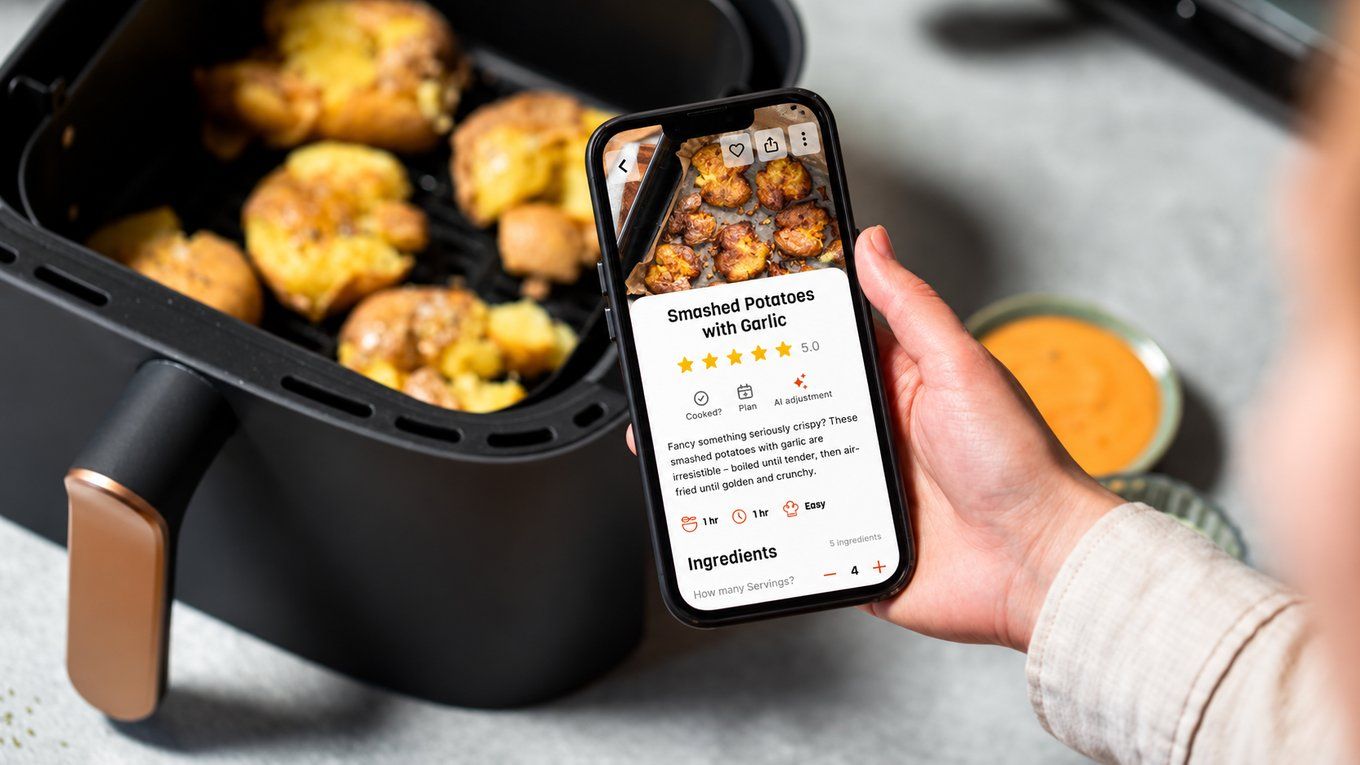 Smashed potatoes with garlic in an air fryer basket, with a phone showing the same recipe as a rated, tested Air Fryer Club recipe card