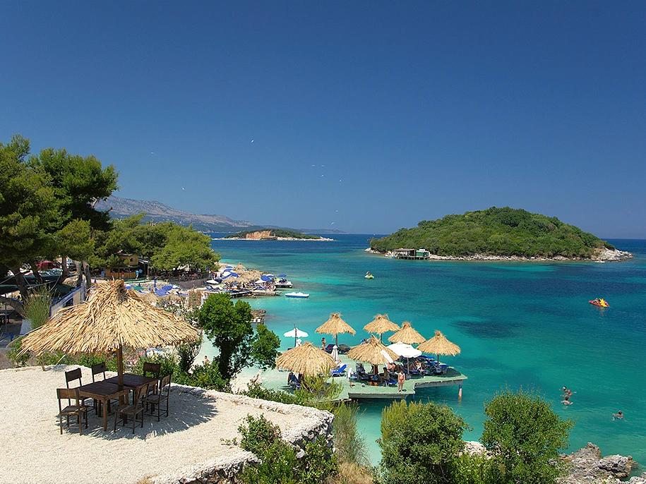 Albanian gravel beach with clear blue water and lush green hills, showcasing the beauty of Albania’s coastal towns