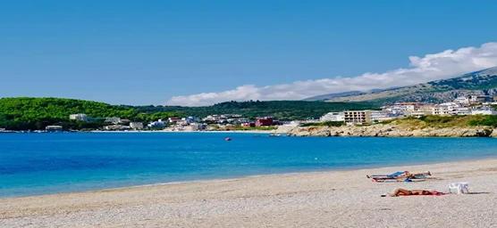 Albanian gravel beach with clear blue water and lush green hills, showcasing the beauty of Albania’s coastal towns