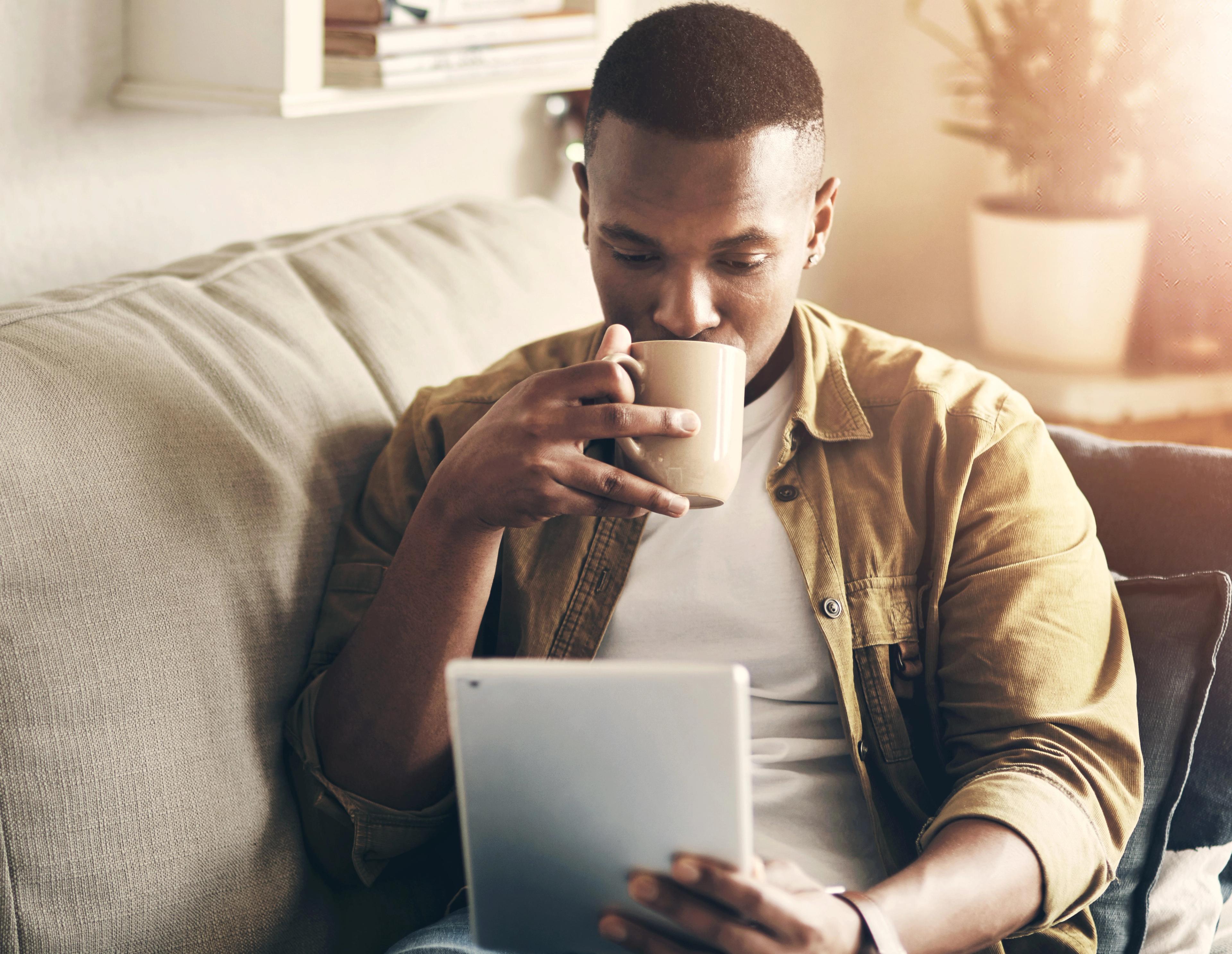 Man sitting on sofa with coffee reading from tablet