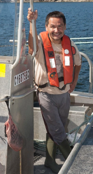 First Nations worker holding a salmon on a farm vessel on the B.C. coast