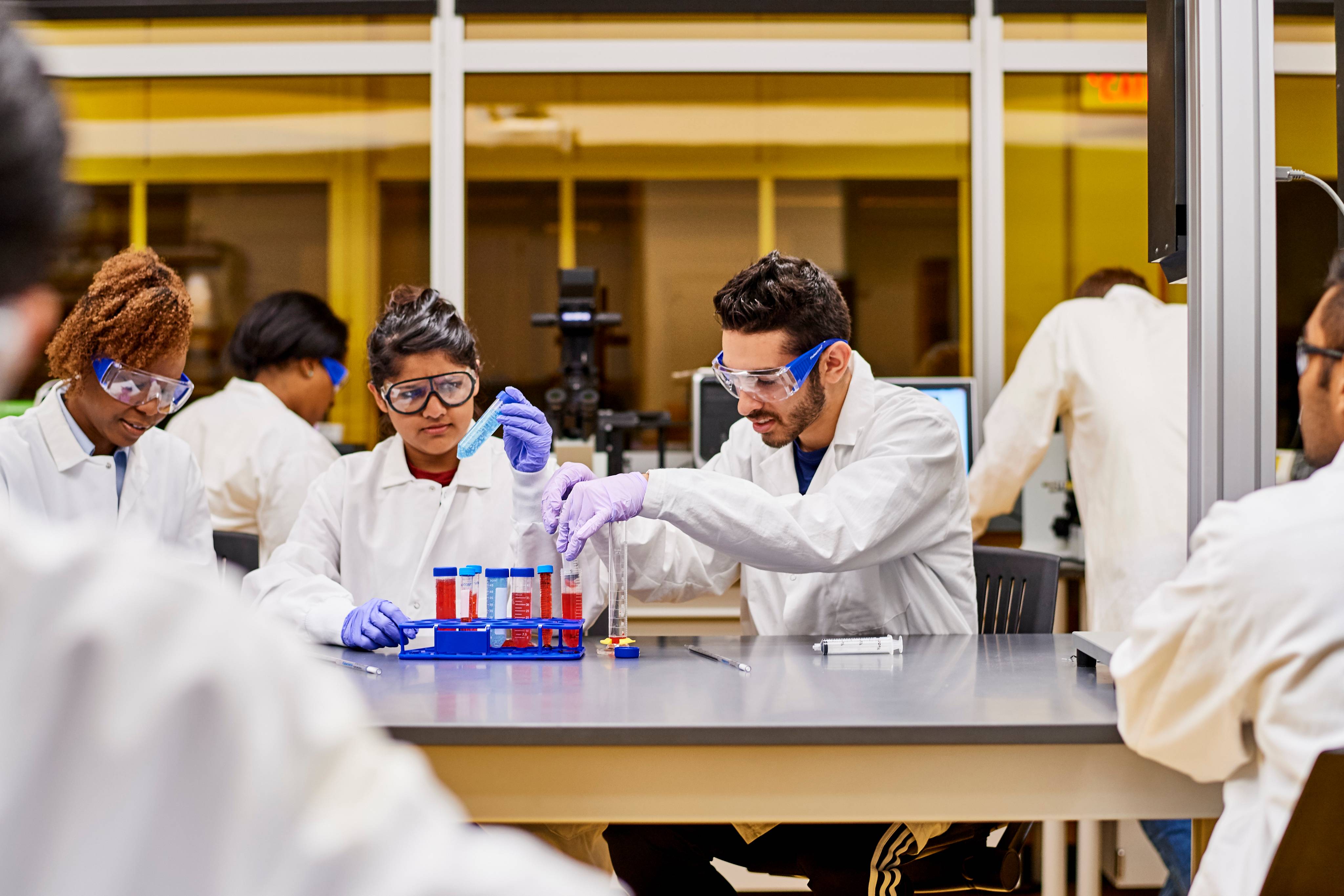 Researchers in lab gear examining liquid in vials