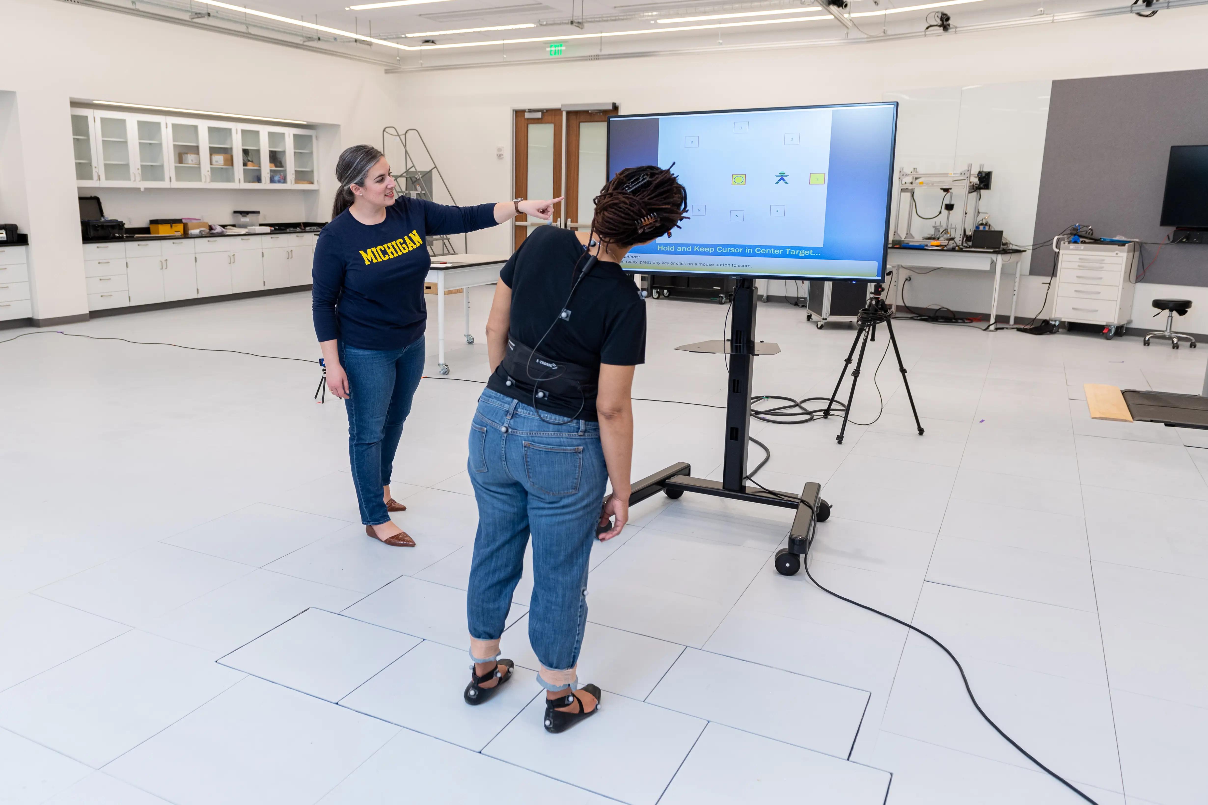 People standing and pointing at a large monitor in the middle of a room