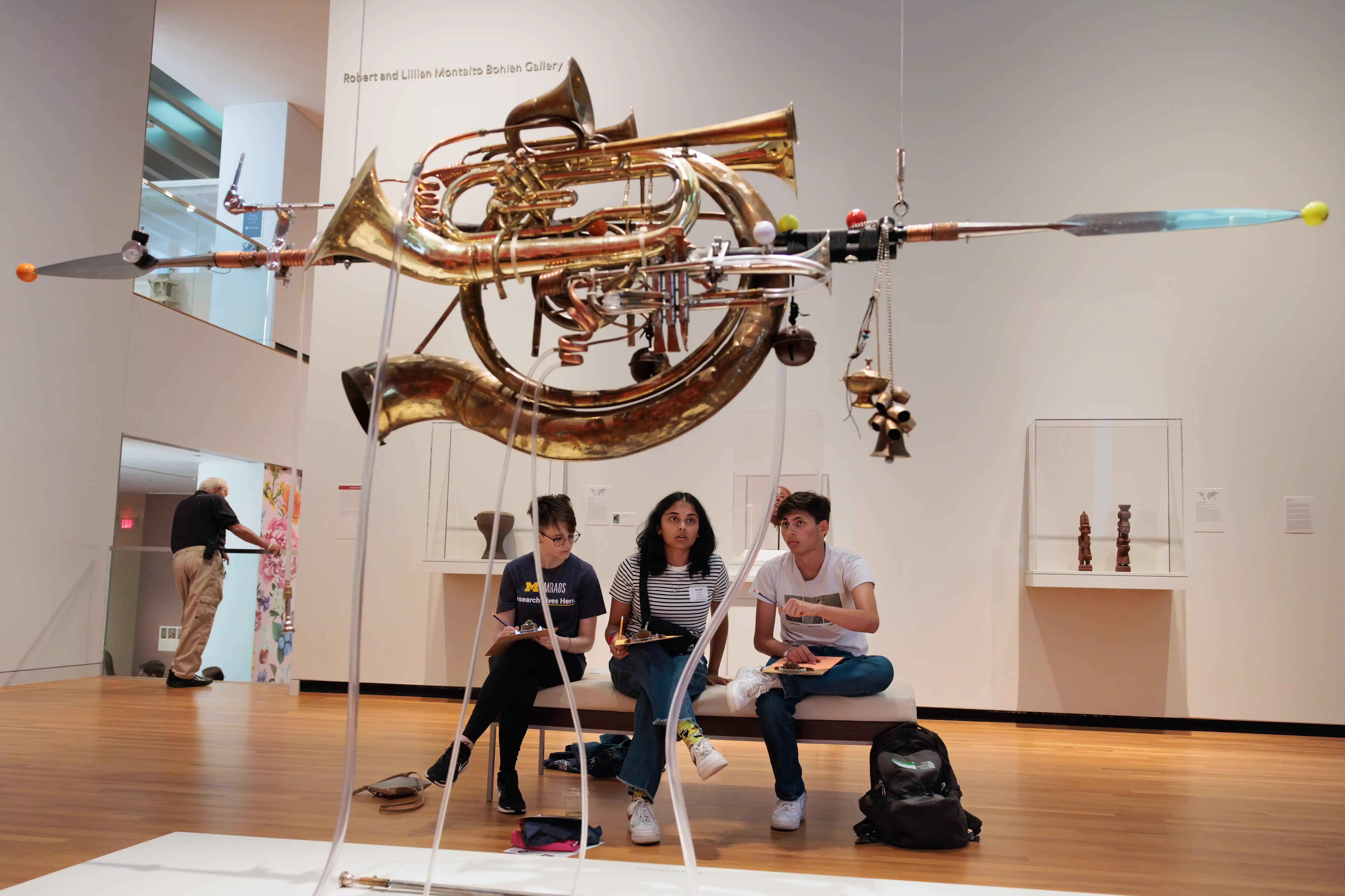 Students sitting under an art installation made of musical instruments at UMMA