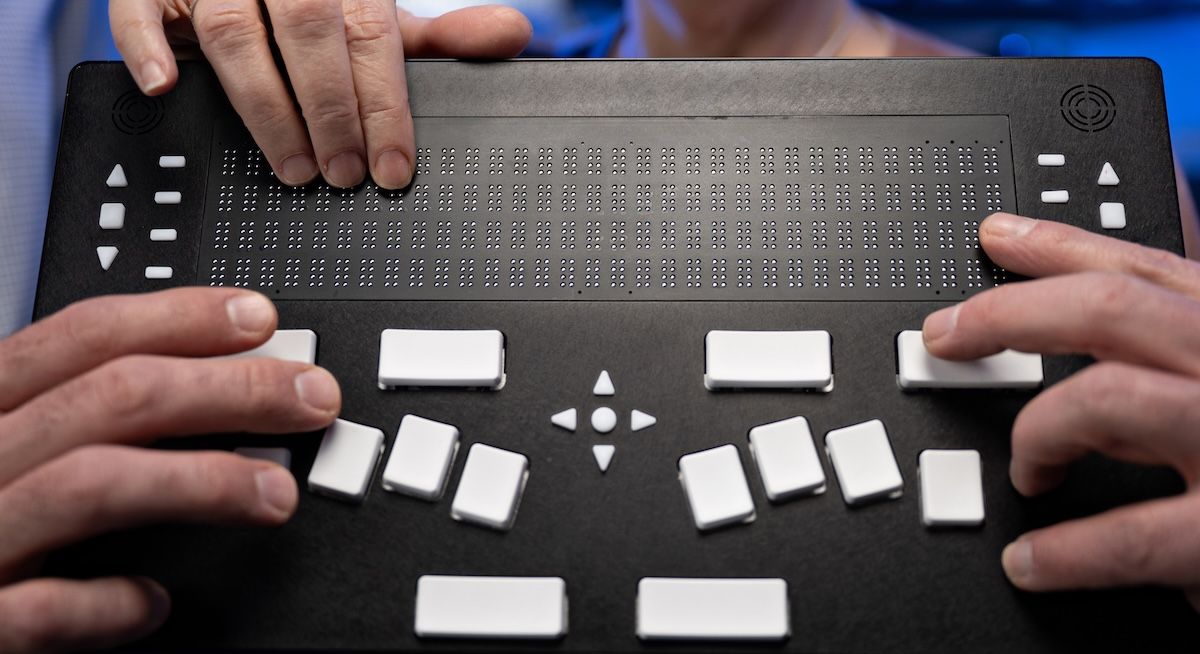 Hands holding the NewHaptics Braille device