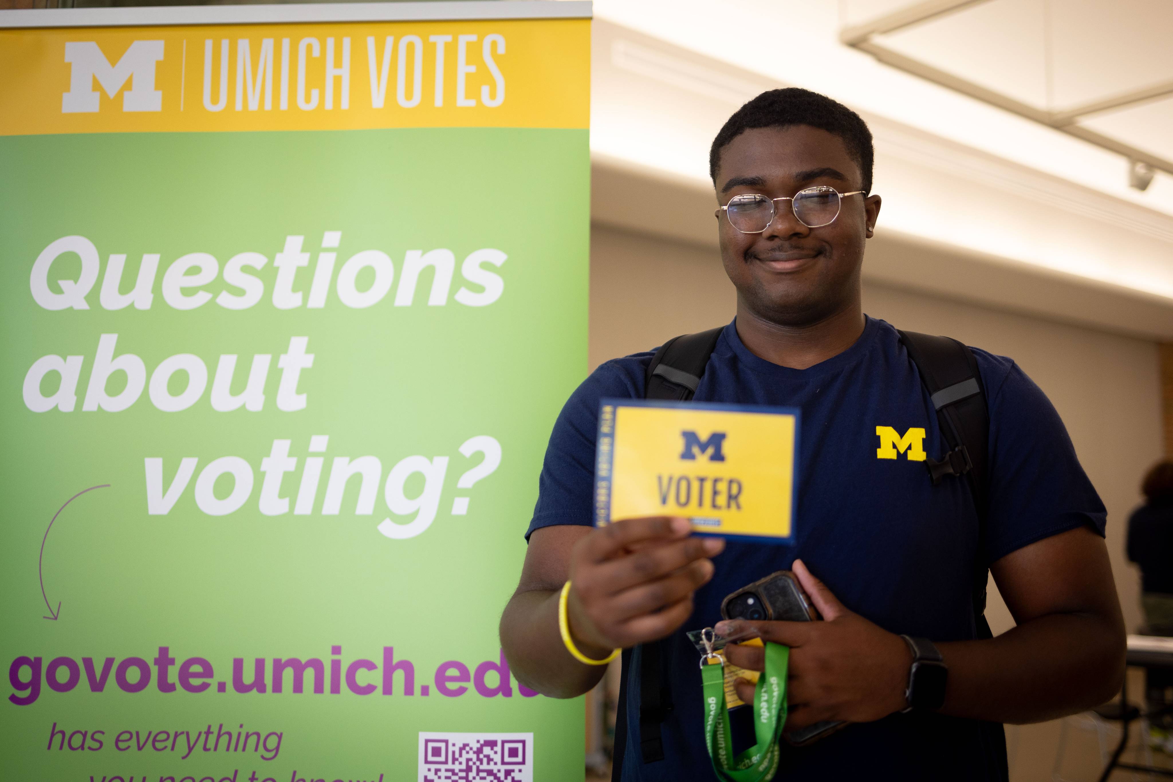 A smiling student walking out of a Umich Votes site carrying a card that says "Voter"