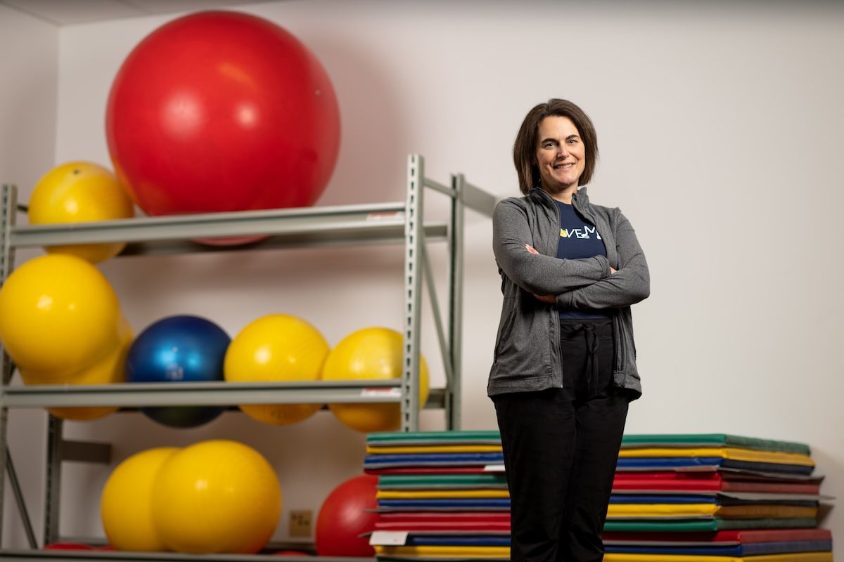 Professor Amy Yorke stands in front of colorful mats and a rack of exercise balls