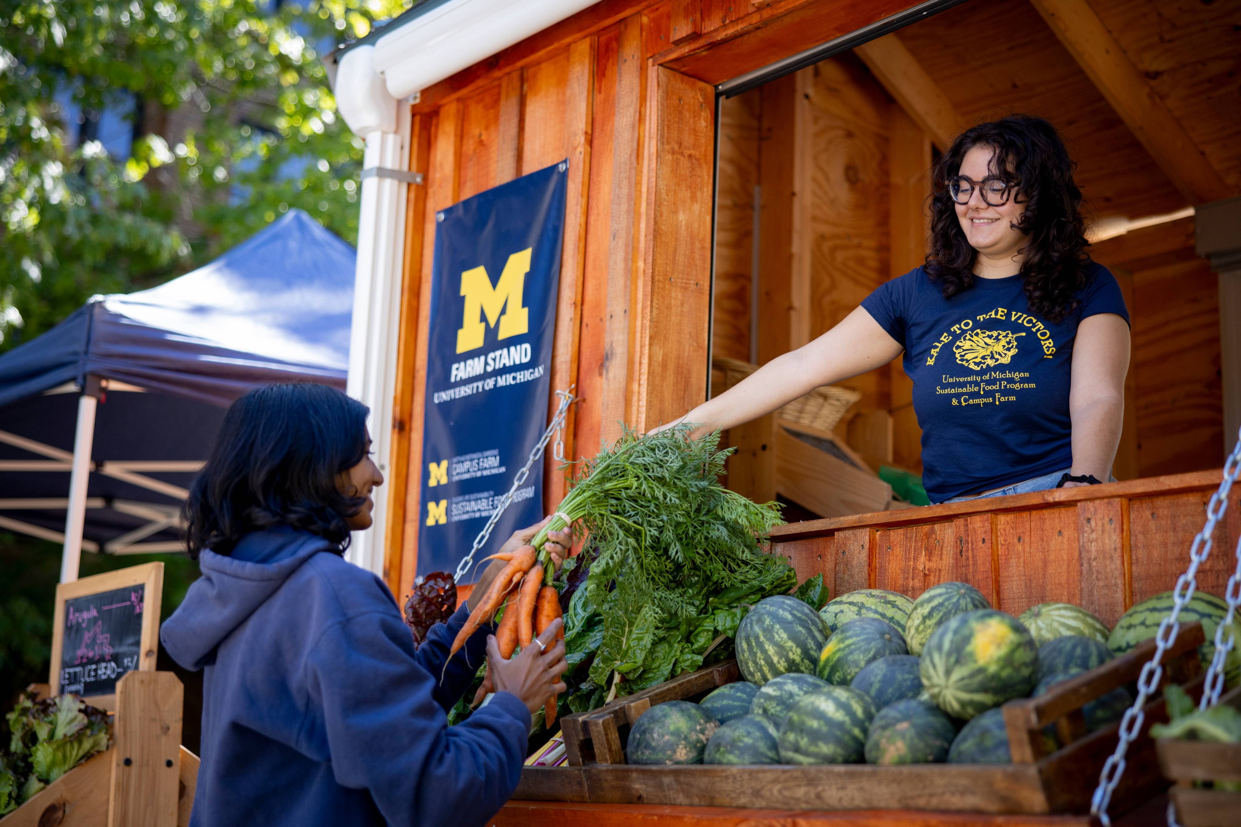A student handing a person carrots at a campus farm stand