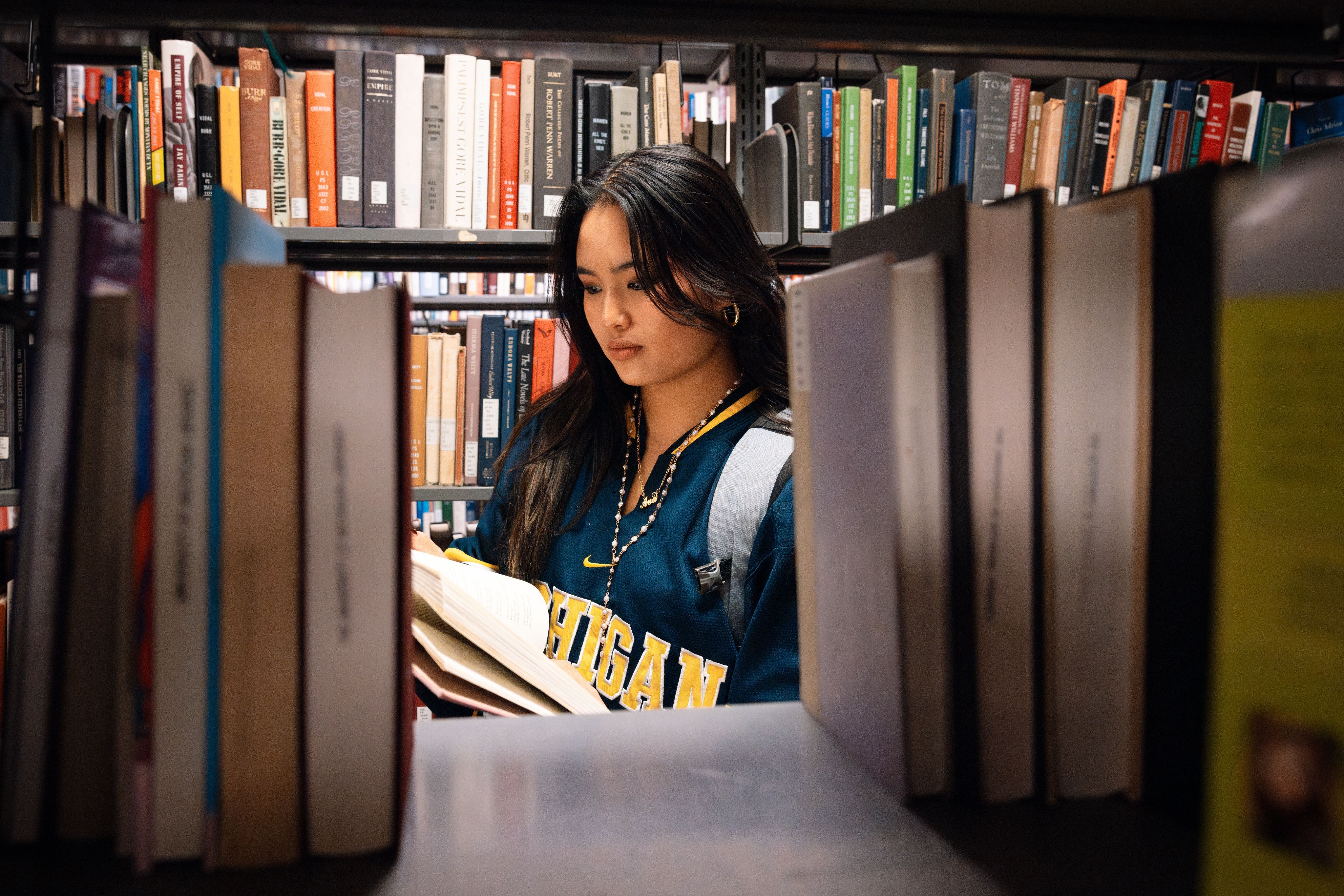 A student reading a book in the stacks