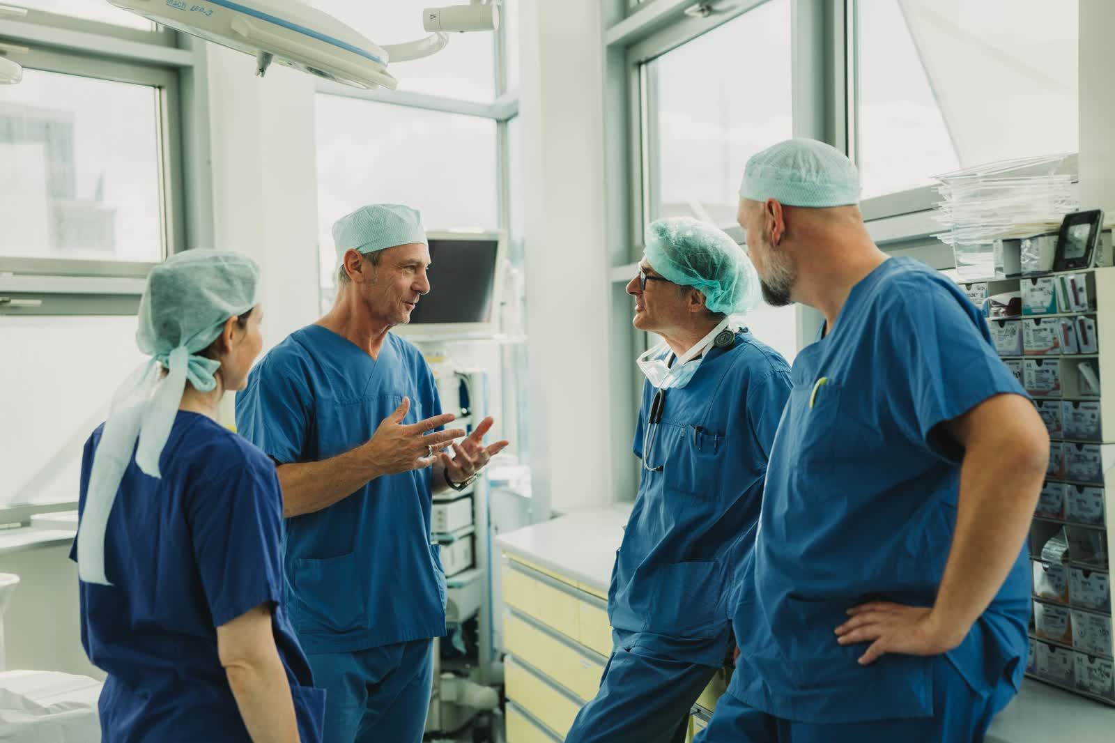 OP-Team in blauer OP-Kleidung und Hauben im Gespräch
