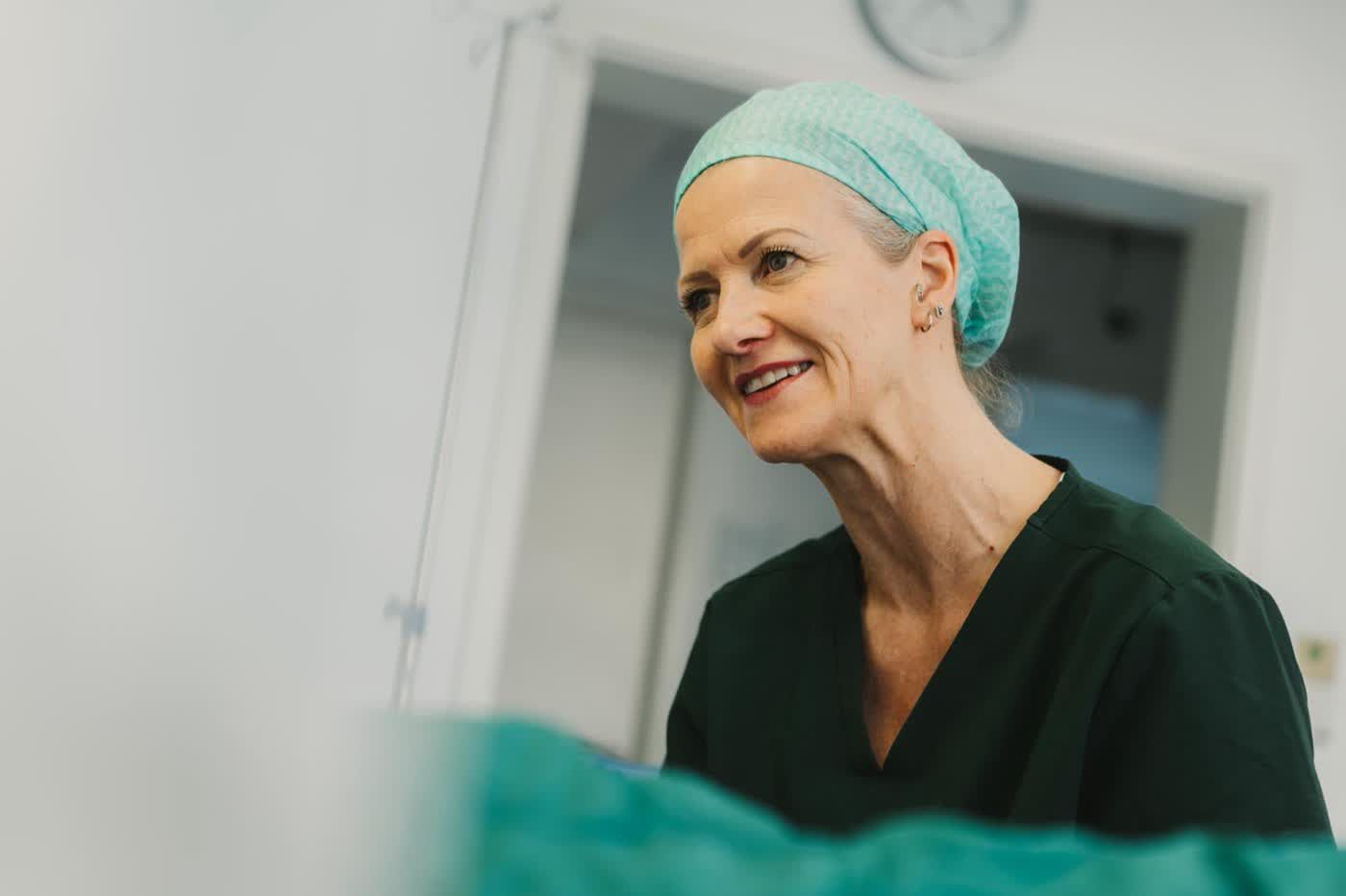 Lächelnde Mitarbeiterin mit OP-Haube und dunkler Klinikkleidung