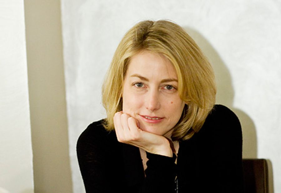 Adele Reising in a black top, her chin resting on her hand, looking directly at the camera against a plain pale wall.