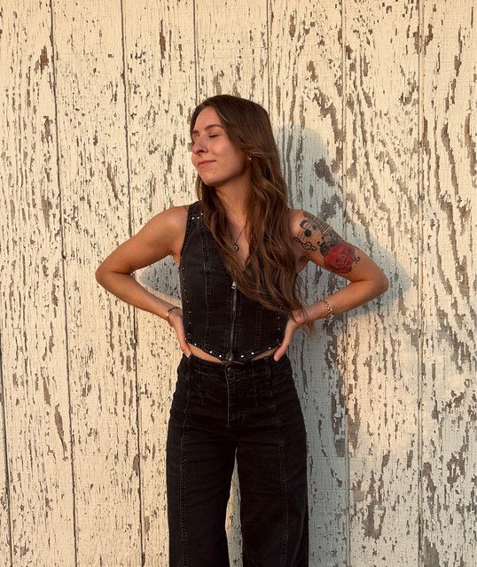 Emily Michelle standing in a black outfit against weathered white wood