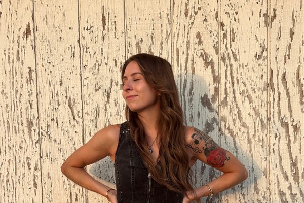 Emily Michelle standing in a black outfit against weathered white wood