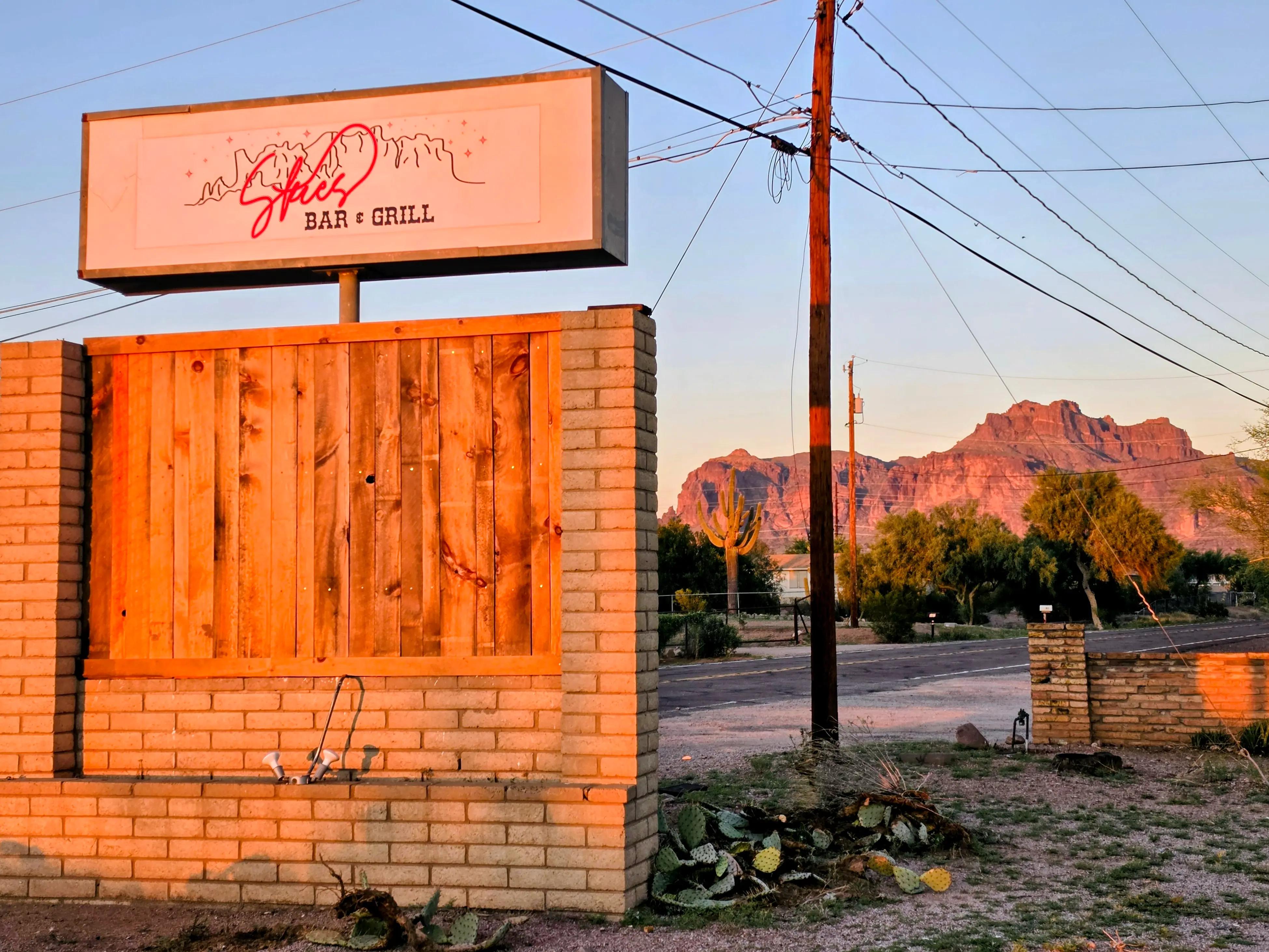 Skies Bar & Grill roadside sign with the Superstition Mountains at sunset.