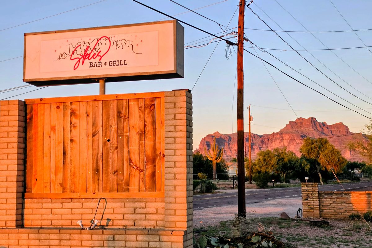 Skies Bar & Grill roadside sign with the Superstition Mountains at sunset.