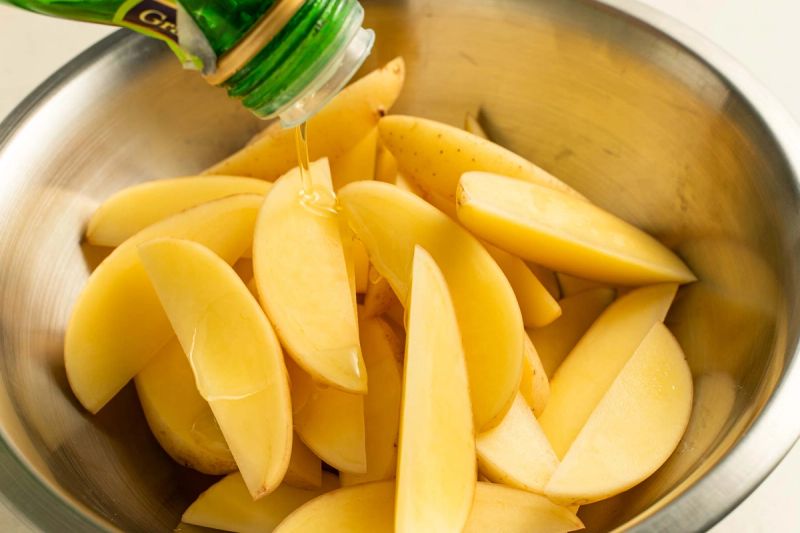 Pouring oil onto potato wedges in a bowl