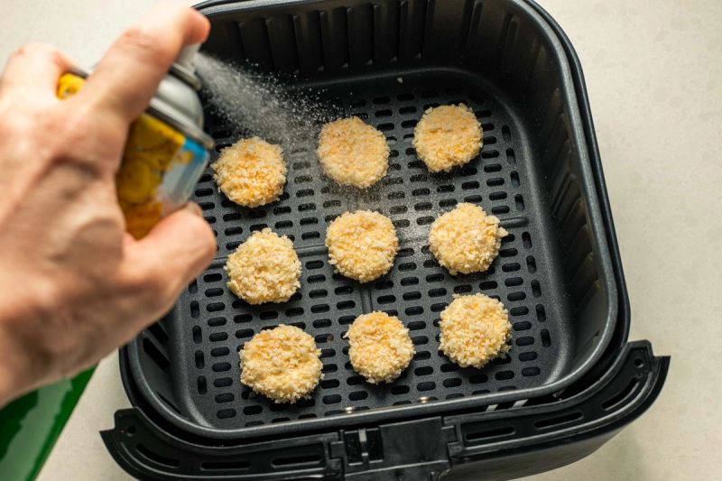 Spraying oil onto breaded goats cheese in air fryer basket