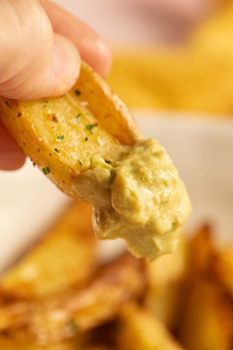 Dipping potato wedge into avocado dip