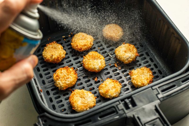 Spraying oil onto semi cooked goats cheese in air fryer basket