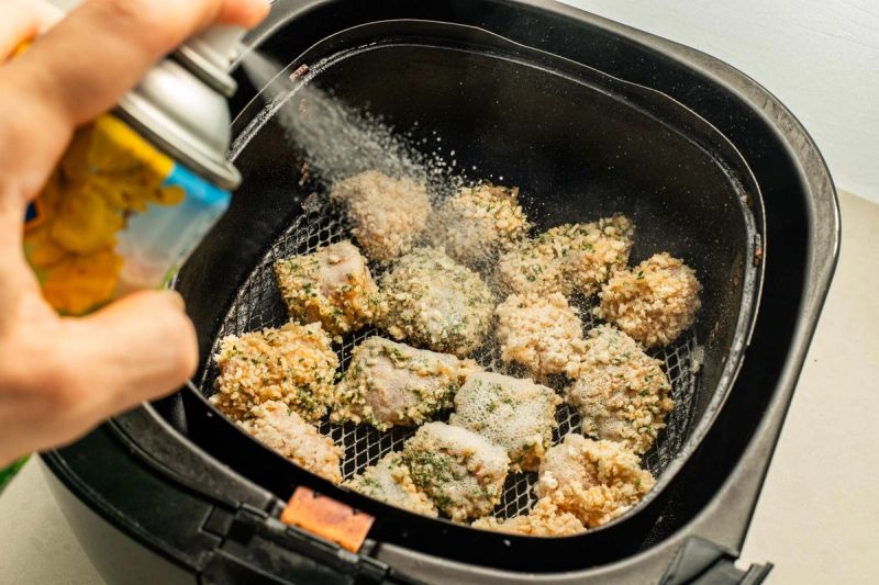 Spraying oil onto chicken in air fryer basket Spraying oil onto chicken in air fryer basket