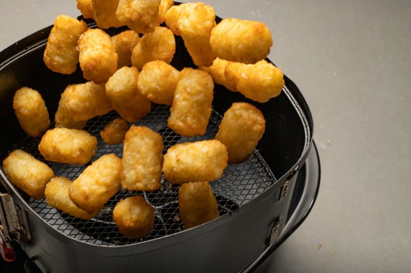 Tossing air fryer basket with potato gems Tossing air fryer basket with potato gems