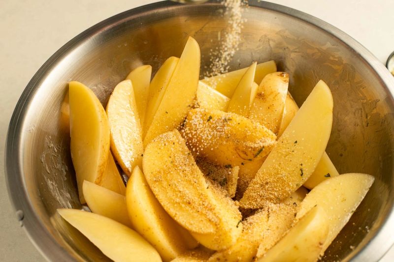 Seasoning potato wedges in a bowl