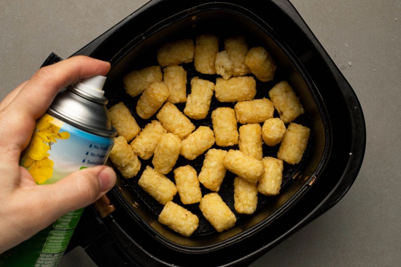 Spraying oil on frozen potato gems in air fryer basket