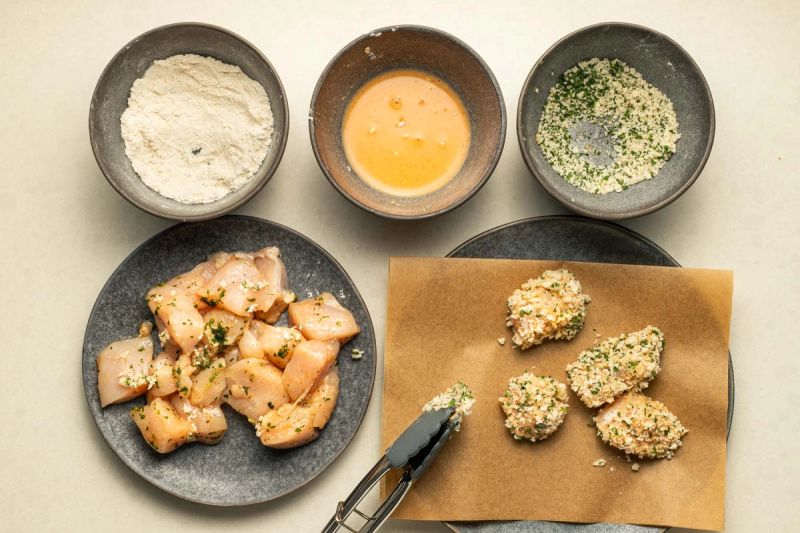Coating raw chicken in flour, egg, and breadcrumbs