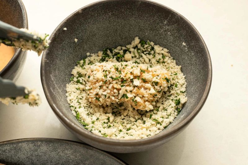 Raw chicken piece coated in breadcrumbs and herbs