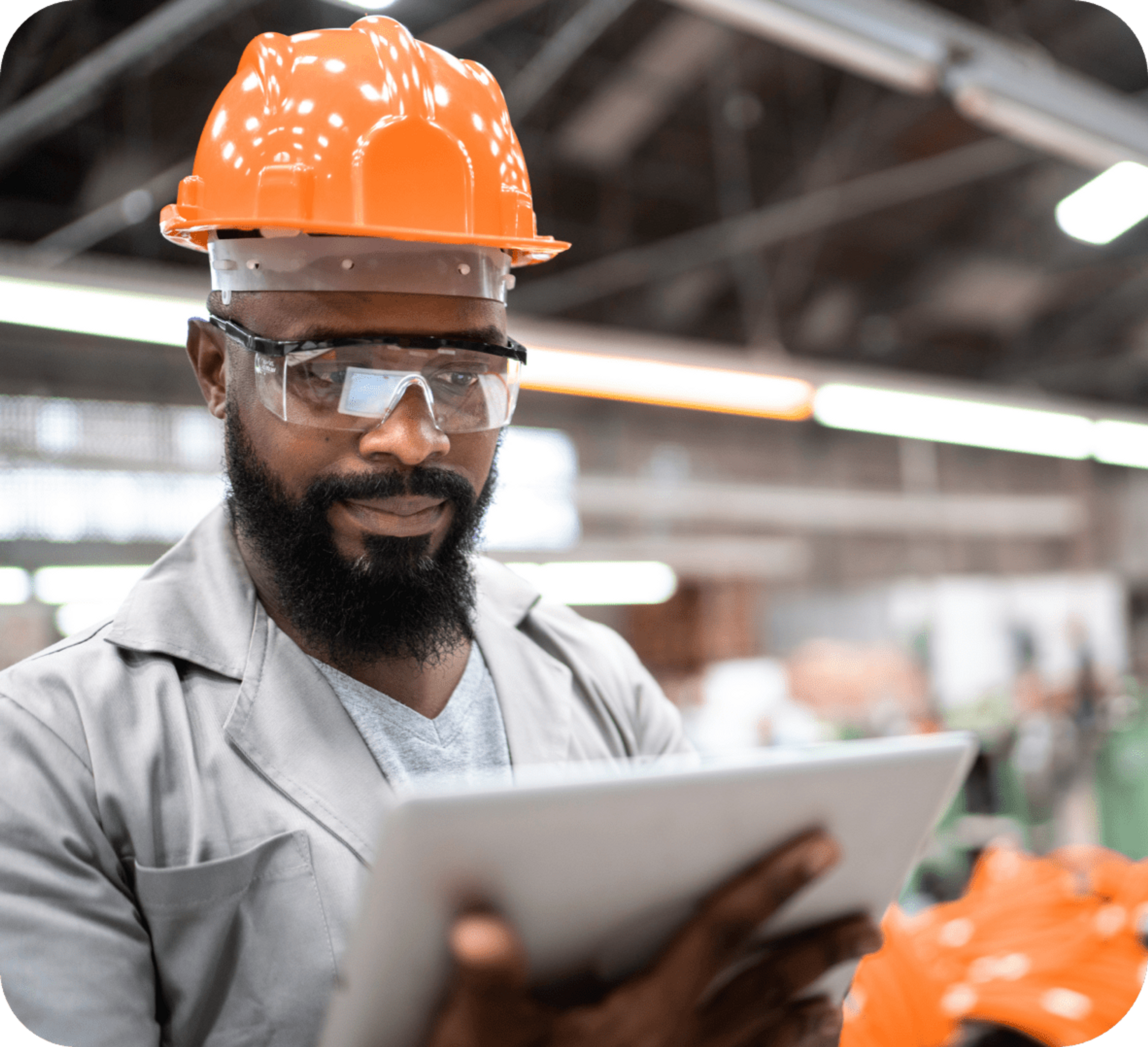 Picture of African man wearing safety glasses, orange hard hat, gray coat and gray t-shirt while holding a white clipboard and seems to be reflecting about the data he is reading on that clipboard