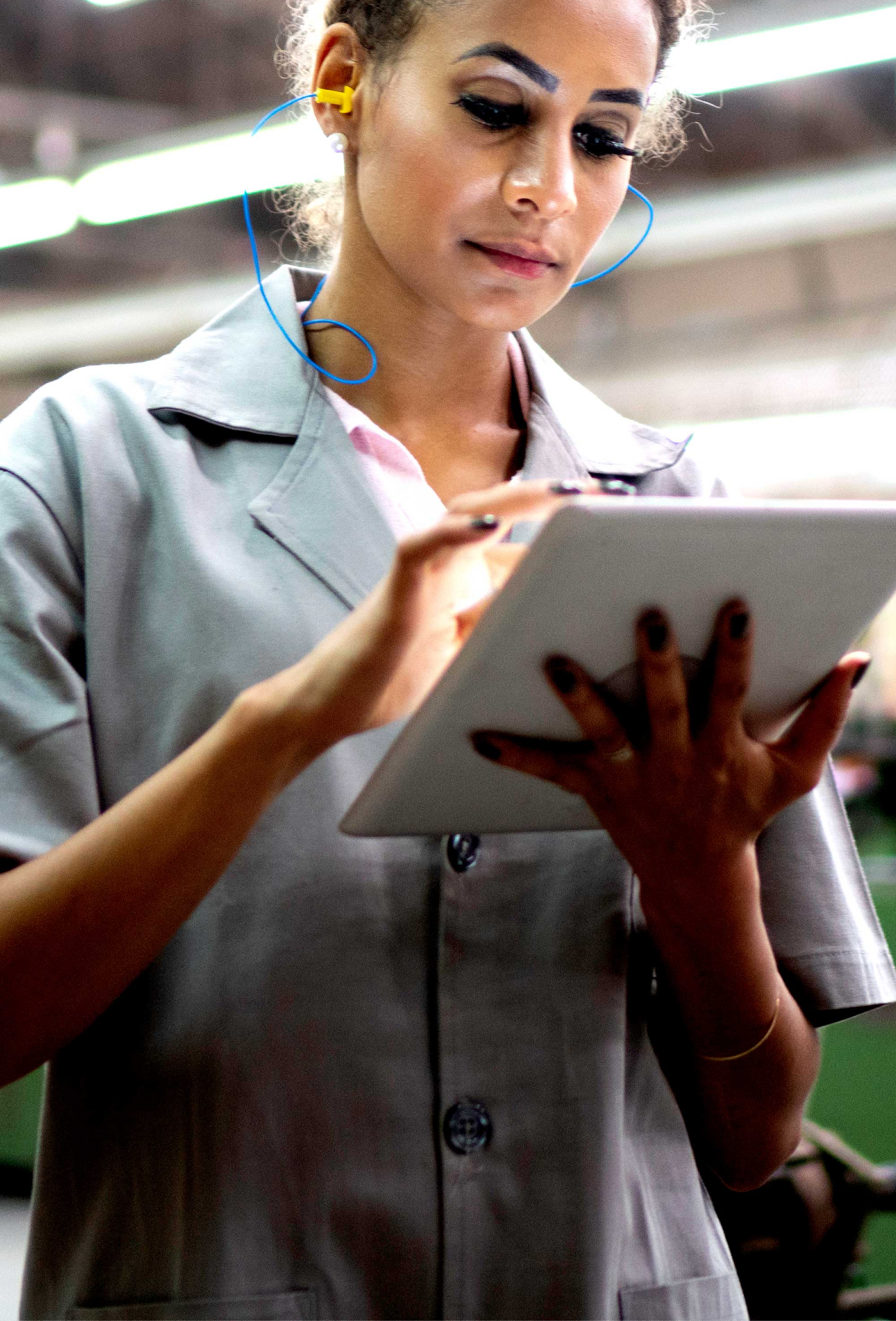 Image of blonde wearing yellow earplugs and  a gray lab coat typing on an ipad