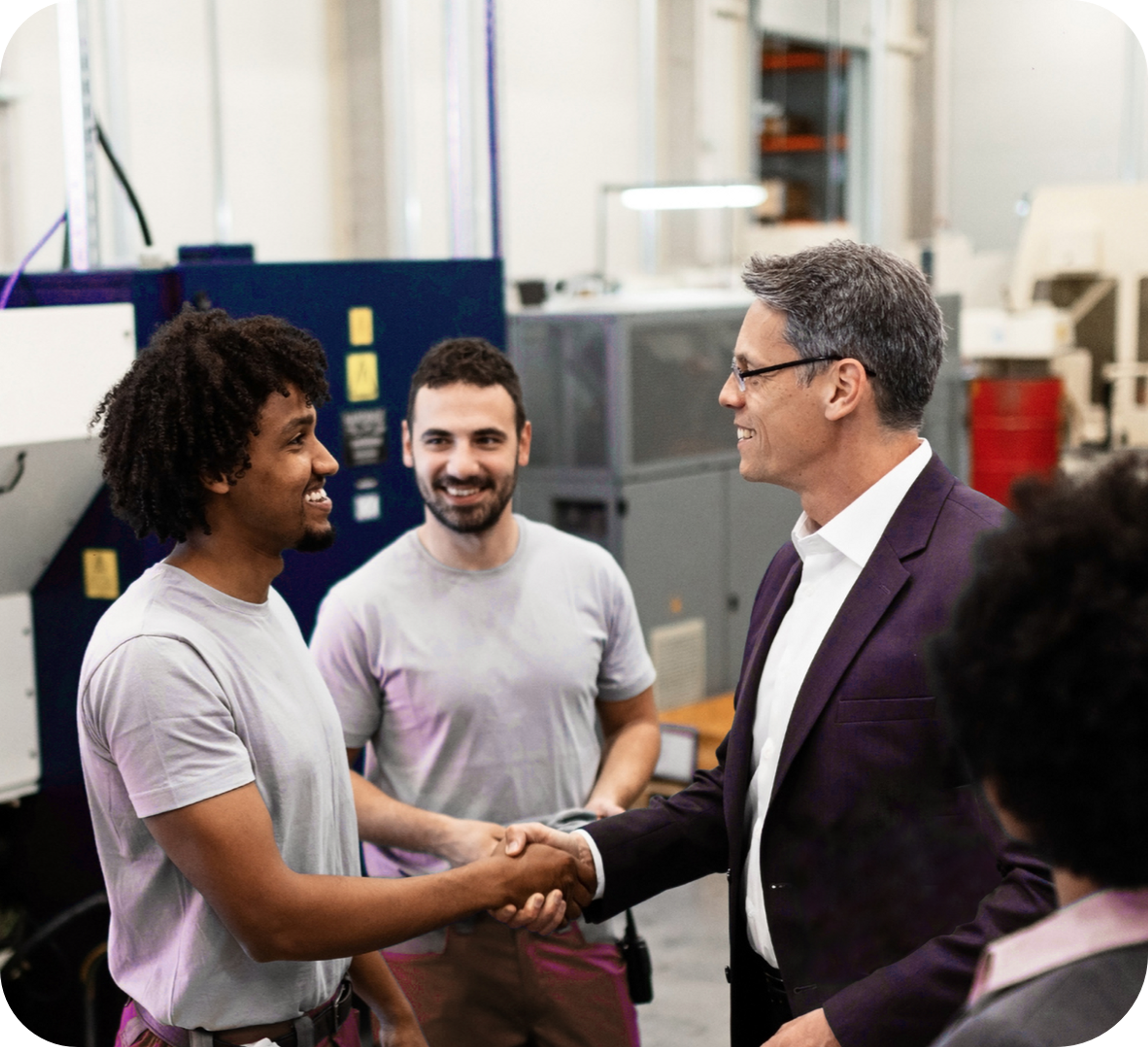 Picture of a middle aged business man shaking hands with an African worker wearing a white t-shirt, while a Caucasian worker with a black beard watches them