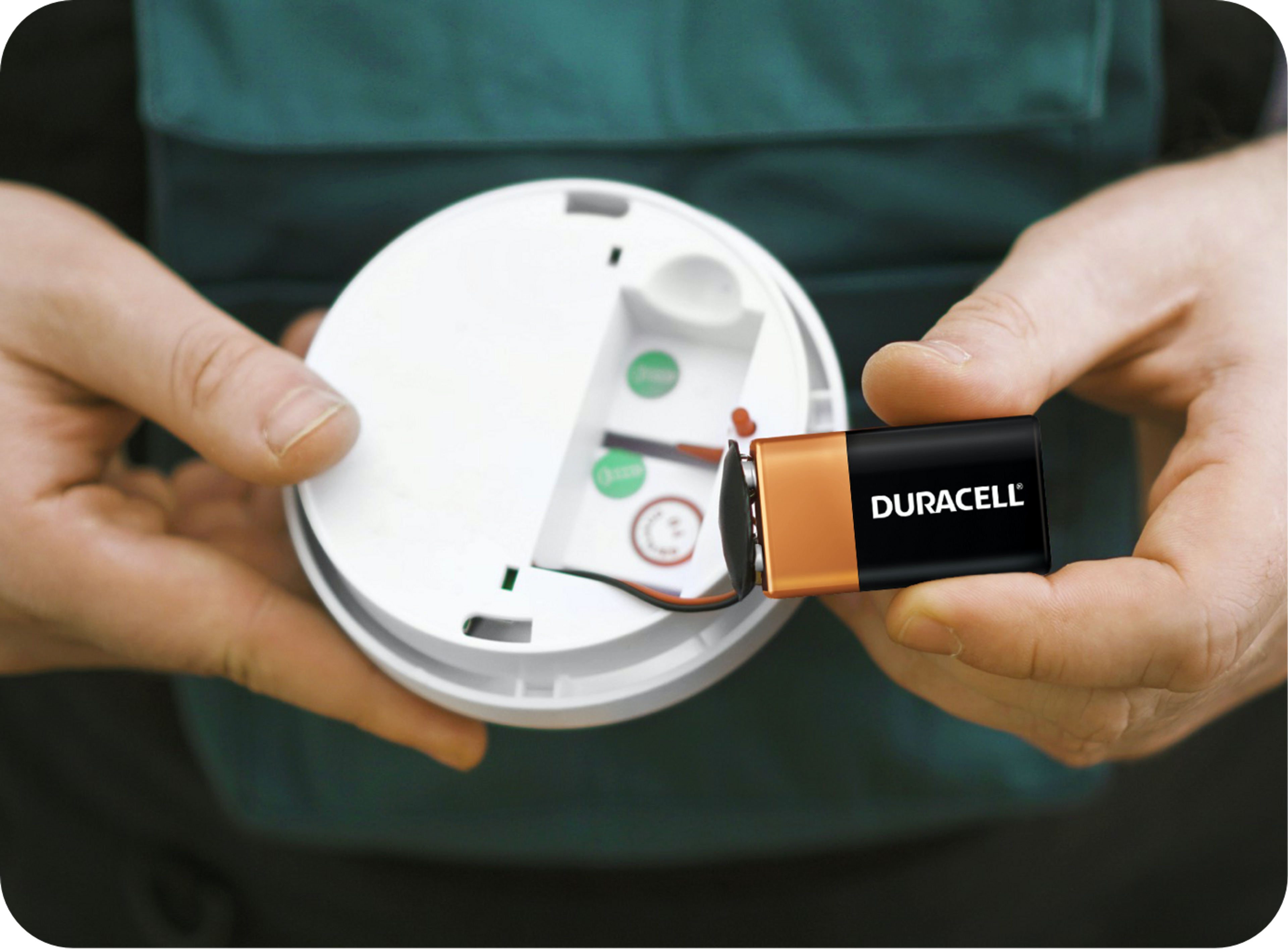 Picture of smoke detector and duracel battery being held by a Caucasian man's hands