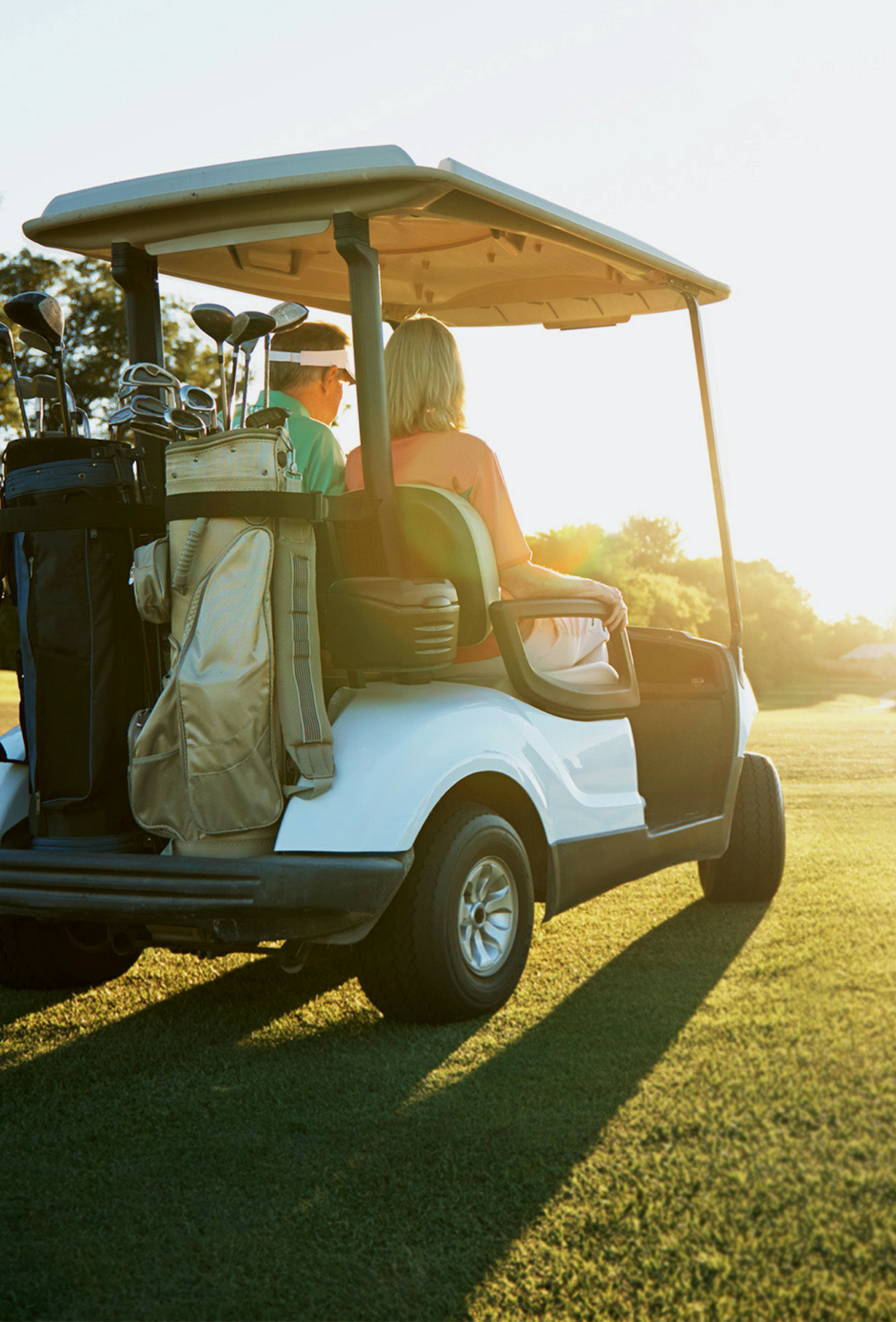 Picture of man and woman driving a golf cart through sunset field