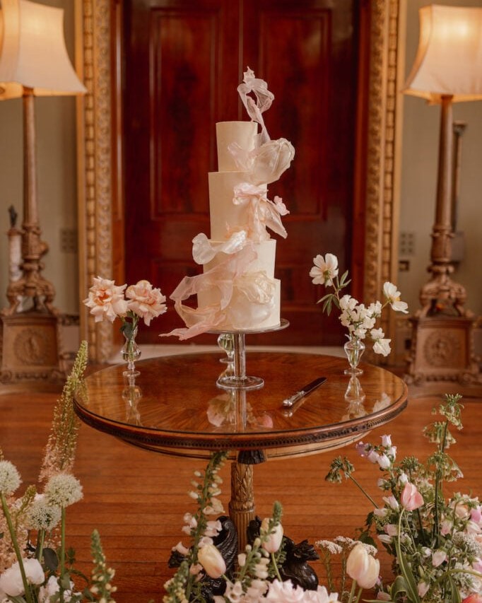 A three-tier, round cake covered in smooth, pale ivory buttercream, featuring delicate, ethereal