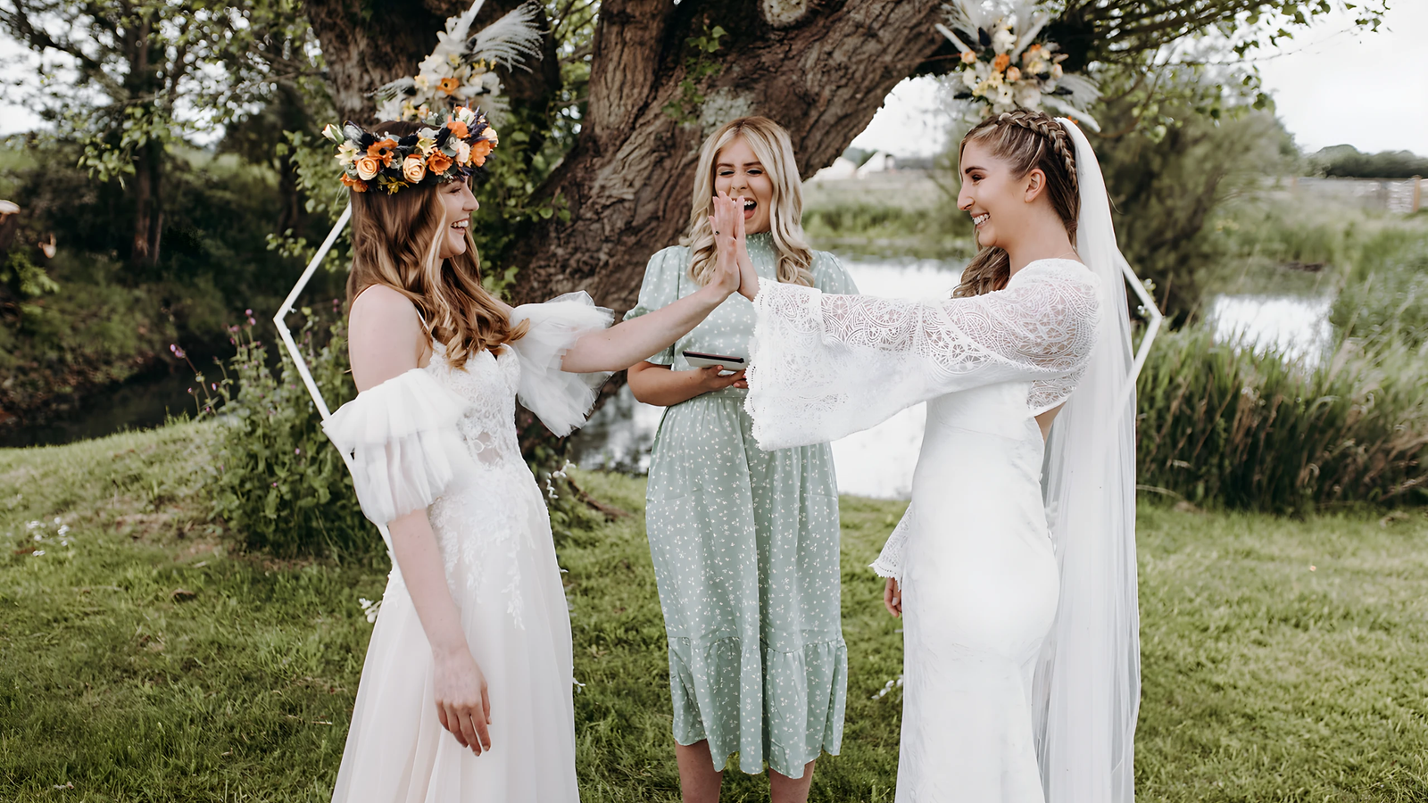 An outdoor ceremony taking place by a small body of water, possibly a pond or stream, with two