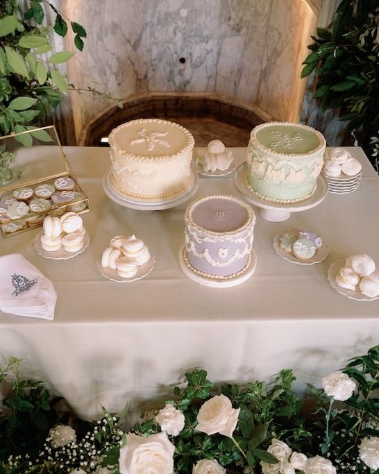A dessert table featuring three single-tier round cakes in pastel colours, alongside various sweet