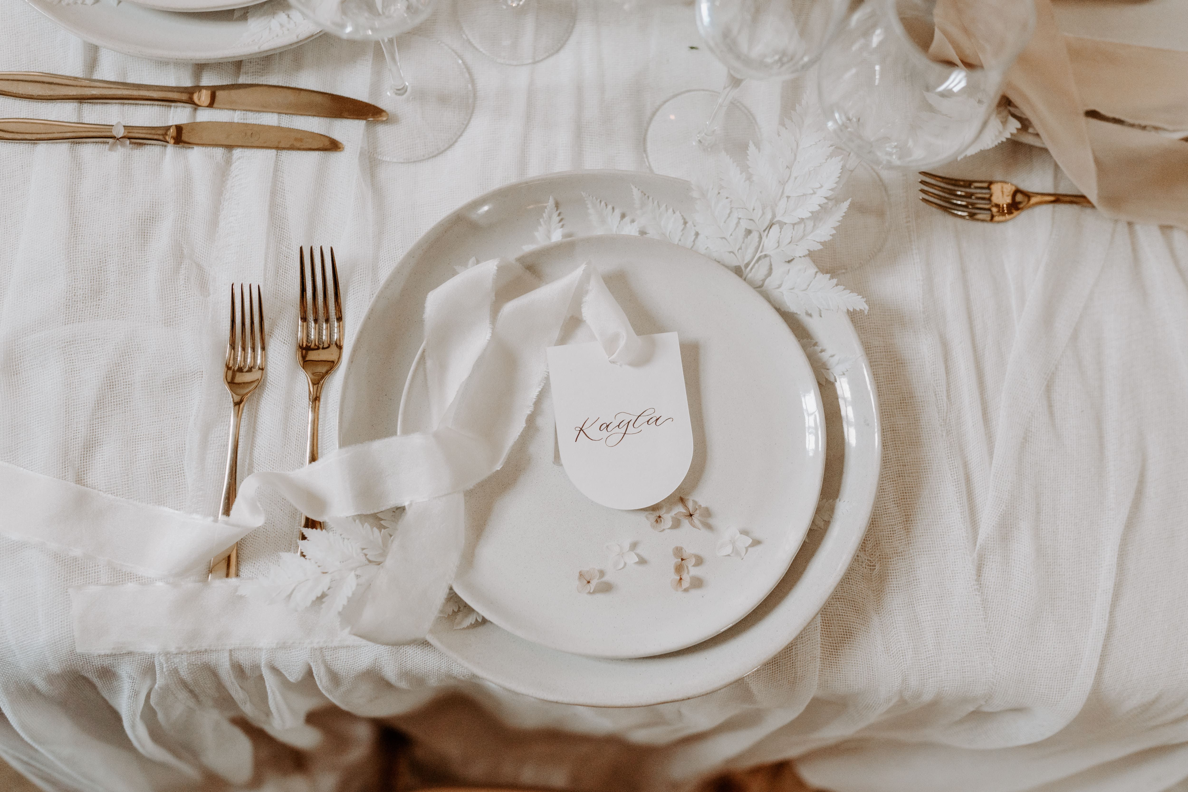 A romantic place card with modern calligraphy, styled on a neutral tablescape. The design features