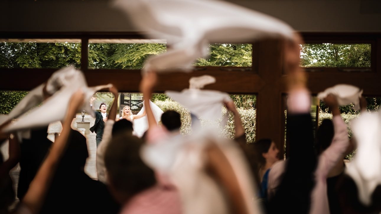 The newly married couple reacts with open-mouthed joy as they are welcomed into a reception room
