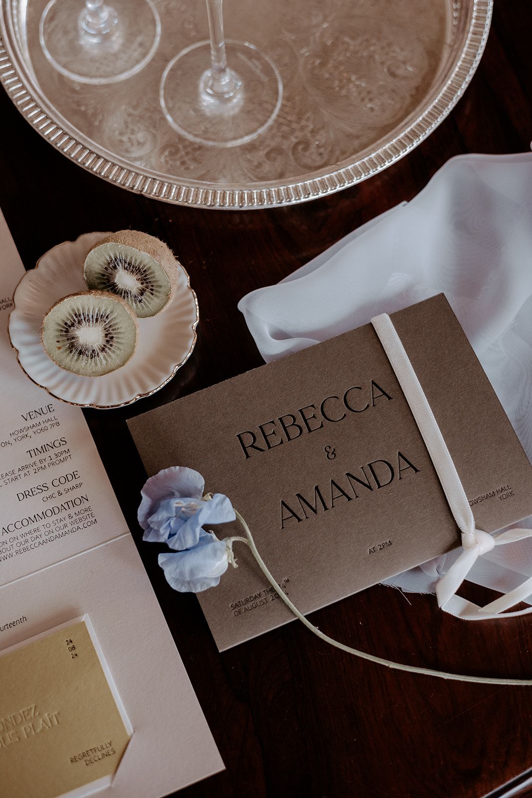 A rustic invitation suite featuring a brown card with embossed sans-serif typography for the